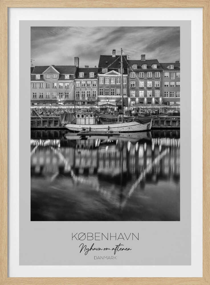 A black and white poster of Nyhavn harbor in Copenhagen at night. Historic buildings with glowing windows line the canal, and their lights create shimmering reflections in the water. A boat is docked in the foreground. The poster has text at the bottom that reads 'KØBENHAVN, Nyhavn om aftenen, DANMARK'. Poster