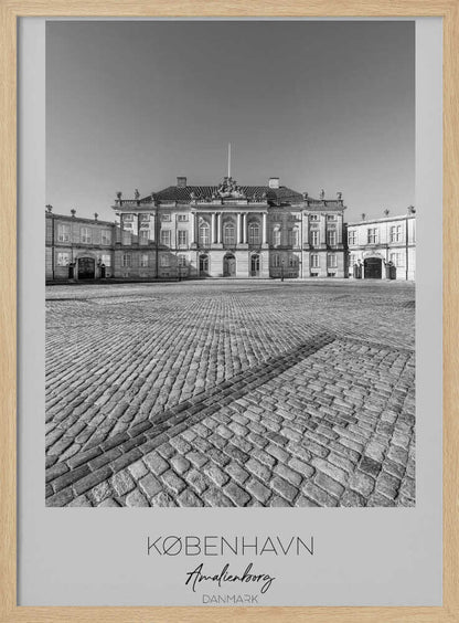 A framed, vertical black and white photograph of Amalienborg Palace in Copenhagen. The shot is taken from a low angle, emphasizing the large cobblestone square in the foreground. The palace stands symmetrically in the background under a clear sky. At the bottom of the poster, text reads 'KØBENHAVN', 'Amalienborg', and 'DANMARK'. Poster