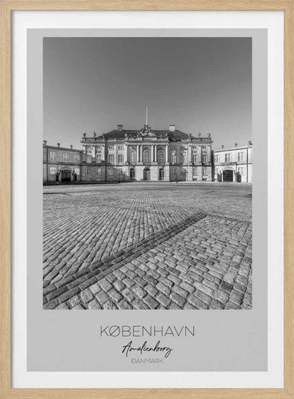 A framed, vertical black and white photograph of Amalienborg Palace in Copenhagen. The shot is taken from a low angle, emphasizing the large cobblestone square in the foreground. The palace stands symmetrically in the background under a clear sky. At the bottom of the poster, text reads 'KØBENHAVN', 'Amalienborg', and 'DANMARK'. Poster