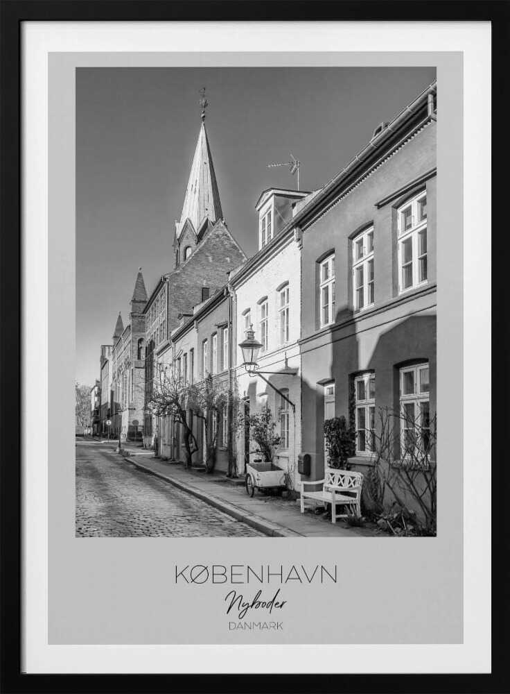 A black and white framed travel poster of a charming cobblestone street in Nyboder, Copenhagen. The photograph shows a sunlit row of historic houses with a prominent church steeple in the background. At the bottom of the poster, the words 'KØBENHAVN', 'Nyboder', and 'DANMARK' are written. Wall Art