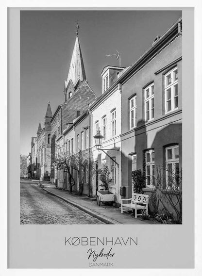 A black and white framed travel poster of a charming cobblestone street in Nyboder, Copenhagen. The photograph shows a sunlit row of historic houses with a prominent church steeple in the background. At the bottom of the poster, the words 'KØBENHAVN', 'Nyboder', and 'DANMARK' are written. Wall Art