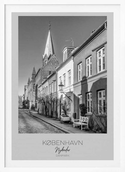 A black and white framed travel poster of a charming cobblestone street in Nyboder, Copenhagen. The photograph shows a sunlit row of historic houses with a prominent church steeple in the background. At the bottom of the poster, the words 'KØBENHAVN', 'Nyboder', and 'DANMARK' are written. Wall Art