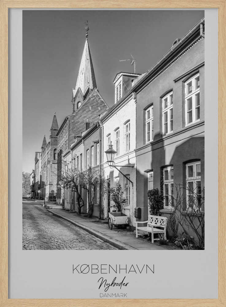 A black and white framed travel poster of a charming cobblestone street in Nyboder, Copenhagen. The photograph shows a sunlit row of historic houses with a prominent church steeple in the background. At the bottom of the poster, the words 'KØBENHAVN', 'Nyboder', and 'DANMARK' are written. Wall Art