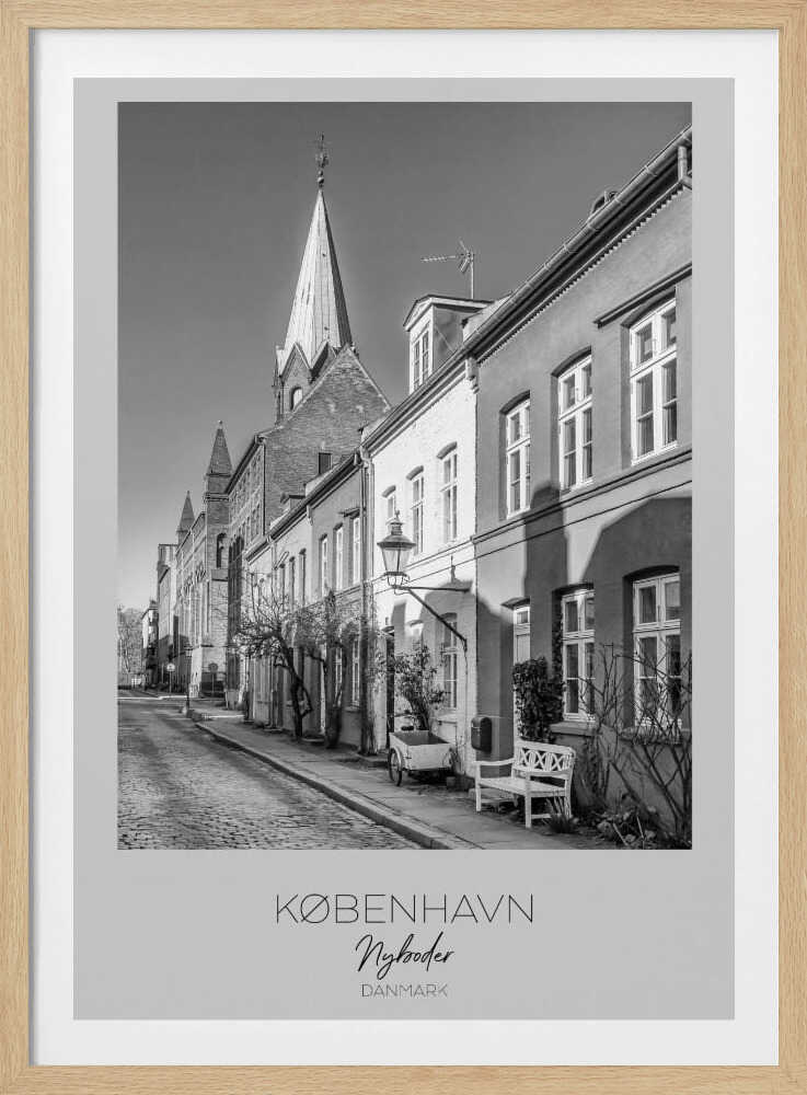 A black and white framed travel poster of a charming cobblestone street in Nyboder, Copenhagen. The photograph shows a sunlit row of historic houses with a prominent church steeple in the background. At the bottom of the poster, the words 'KØBENHAVN', 'Nyboder', and 'DANMARK' are written. Wall Art