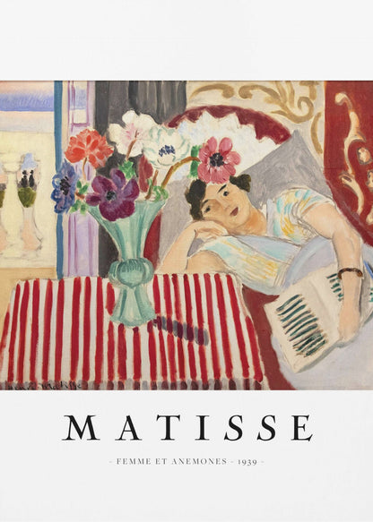 A poster featuring Henri Matisse's 1939 painting, 'Femme et Anemones'. The artwork depicts a woman in a colorful top reclining on a couch, holding a book. Beside her, on a red and white striped tablecloth, sits a vase filled with vibrant anemone flowers. The poster has a black frame and white matting, with 'MATISSE' printed below the image. Artwork