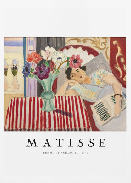 A poster featuring Henri Matisse's 1939 painting, 'Femme et Anemones'. The artwork depicts a woman in a colorful top reclining on a couch, holding a book. Beside her, on a red and white striped tablecloth, sits a vase filled with vibrant anemone flowers. The poster has a black frame and white matting, with 'MATISSE' printed below the image. Artwork