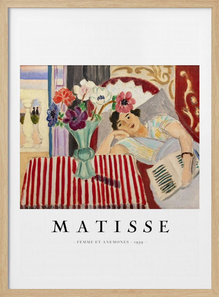 A poster featuring Henri Matisse's 1939 painting, 'Femme et Anemones'. The artwork depicts a woman in a colorful top reclining on a couch, holding a book. Beside her, on a red and white striped tablecloth, sits a vase filled with vibrant anemone flowers. The poster has a black frame and white matting, with 'MATISSE' printed below the image. Artwork