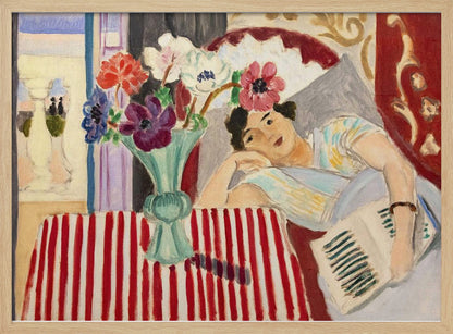A Fauvist-style painting by Henri Matisse depicting a woman in a colorful blouse reclining with a book. Beside her is a table with a bold red-and-white striped cloth holding a light green vase with red, purple, and white anemone flowers. Print