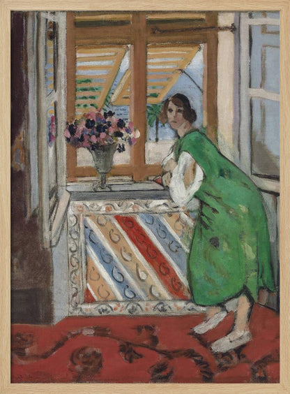 A painting by Henri Matisse depicting a woman in a loose green dress leaning on a windowsill and looking towards the viewer. Outside the open window with tan shutters, a sunny scene with a palm tree is visible. A vase of flowers sits on the sill above a colorful striped panel, and a red patterned rug covers the floor. Print