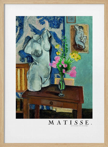 A framed art print of Henri Matisse's painting 'Le Torse en Plâtre'. The still life features a white plaster female torso sculpture next to a dark brown wooden table with a vase of pink and yellow flowers. The background consists of a blue and white patterned tapestry and a teal wall with a small framed nude drawing. Print