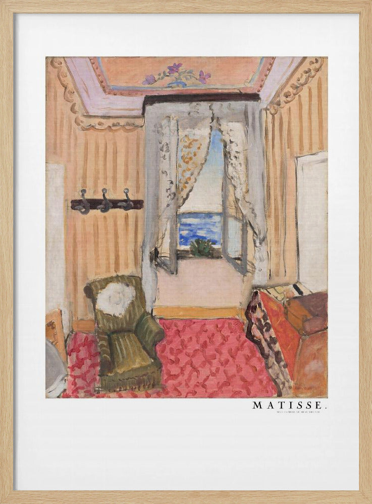 A framed print of a painting by Henri Matisse. The artwork depicts an interior room scene with peach-colored walls, a vibrant pink and red patterned rug, and an armchair. An open window with lace curtains offers a view of the blue sea. Decor