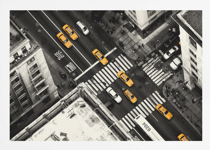 An aerial, black and white photograph of a bustling New York City intersection, with the iconic yellow taxi cabs highlighted in a vibrant selective color. Pedestrians cross the street as cars and a bus navigate the busy roads between tall buildings. Wall Art