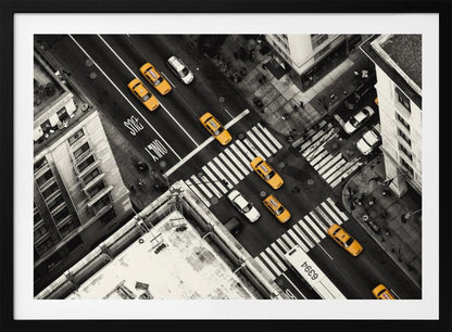 An aerial, black and white photograph of a bustling New York City intersection, with the iconic yellow taxi cabs highlighted in a vibrant selective color. Pedestrians cross the street as cars and a bus navigate the busy roads between tall buildings. Wall Art