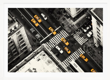 An aerial, black and white photograph of a bustling New York City intersection, with the iconic yellow taxi cabs highlighted in a vibrant selective color. Pedestrians cross the street as cars and a bus navigate the busy roads between tall buildings. Wall Art