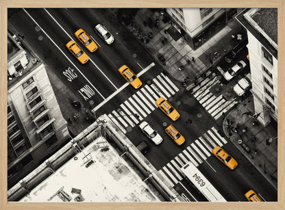 An aerial, black and white photograph of a bustling New York City intersection, with the iconic yellow taxi cabs highlighted in a vibrant selective color. Pedestrians cross the street as cars and a bus navigate the busy roads between tall buildings. Wall Art