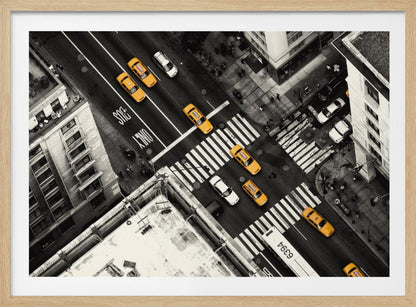 An aerial, black and white photograph of a bustling New York City intersection, with the iconic yellow taxi cabs highlighted in a vibrant selective color. Pedestrians cross the street as cars and a bus navigate the busy roads between tall buildings. Wall Art