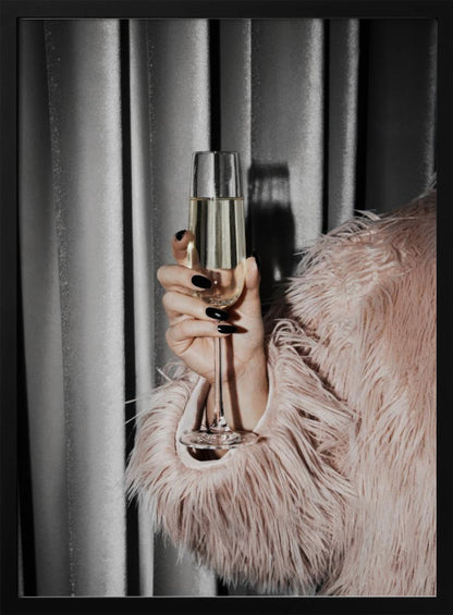 A close-up photograph of a woman's hand with black nail polish holding a tall, elegant flute of champagne. She is wearing a soft, shaggy pink faux fur coat, with a silver-gray curtain in the background, creating a luxurious and celebratory mood. Print