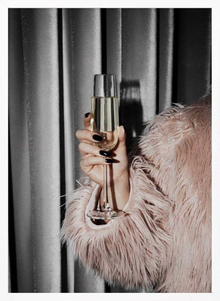 A close-up photograph of a woman's hand with black nail polish holding a tall, elegant flute of champagne. She is wearing a soft, shaggy pink faux fur coat, with a silver-gray curtain in the background, creating a luxurious and celebratory mood. Print