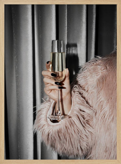 A close-up photograph of a woman's hand with black nail polish holding a tall, elegant flute of champagne. She is wearing a soft, shaggy pink faux fur coat, with a silver-gray curtain in the background, creating a luxurious and celebratory mood. Print