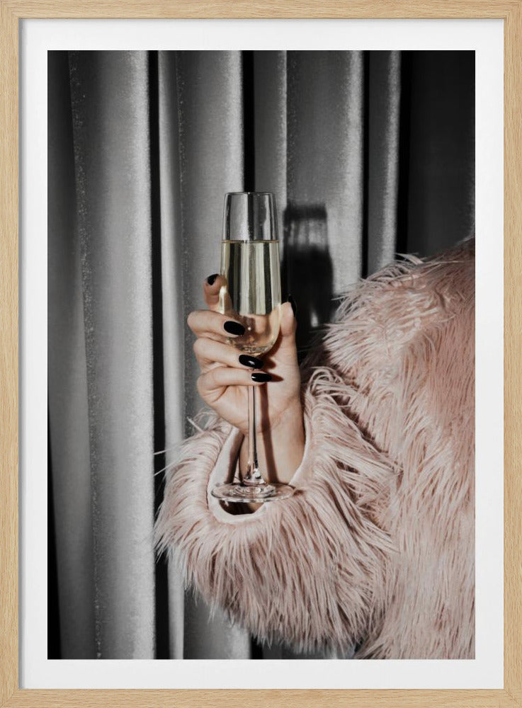 A close-up photograph of a woman's hand with black nail polish holding a tall, elegant flute of champagne. She is wearing a soft, shaggy pink faux fur coat, with a silver-gray curtain in the background, creating a luxurious and celebratory mood. Print