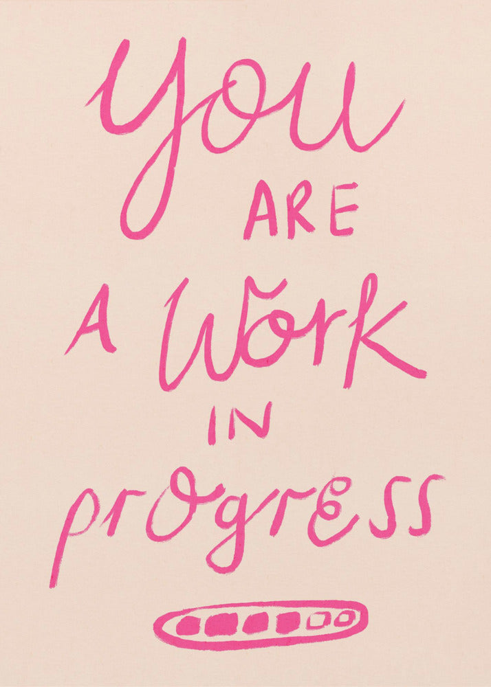 A framed art print featuring the motivational quote 'You are a work in progress'. The text is rendered in a vibrant pink, hand-lettered style against a soft beige background. The words 'You', 'a Work', and 'progress' are in a flowing script, while 'are' and 'in' are in a simple uppercase font. Wall Art