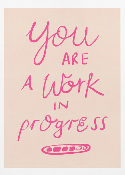 A framed art print featuring the motivational quote 'You are a work in progress'. The text is rendered in a vibrant pink, hand-lettered style against a soft beige background. The words 'You', 'a Work', and 'progress' are in a flowing script, while 'are' and 'in' are in a simple uppercase font. Wall Art