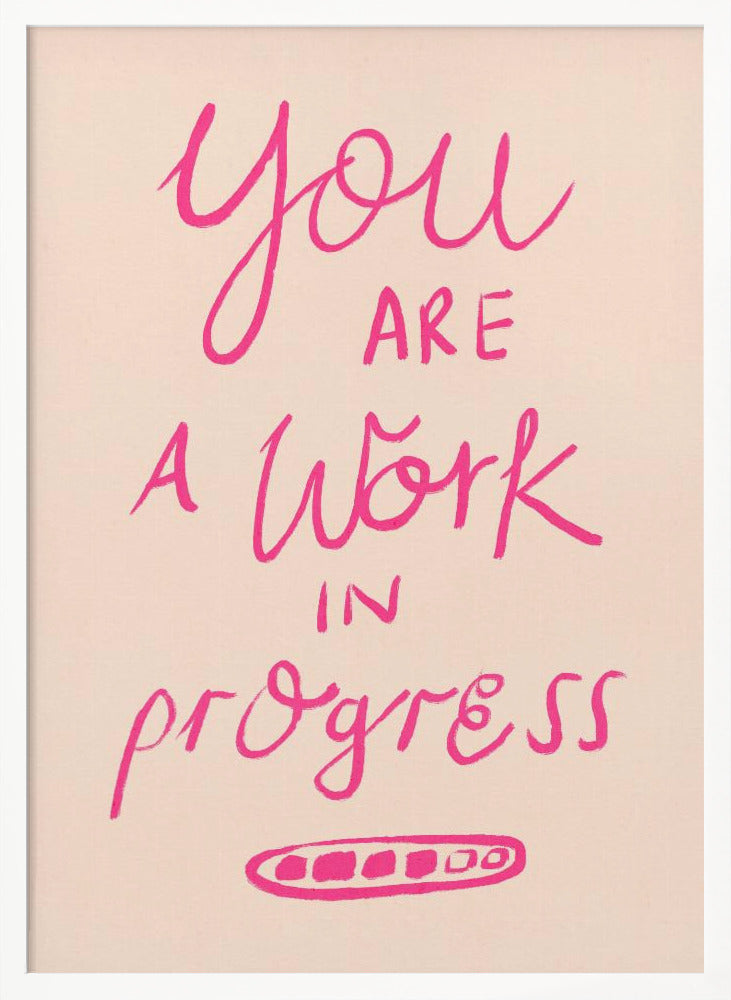 A framed art print featuring the motivational quote 'You are a work in progress'. The text is rendered in a vibrant pink, hand-lettered style against a soft beige background. The words 'You', 'a Work', and 'progress' are in a flowing script, while 'are' and 'in' are in a simple uppercase font. Wall Art