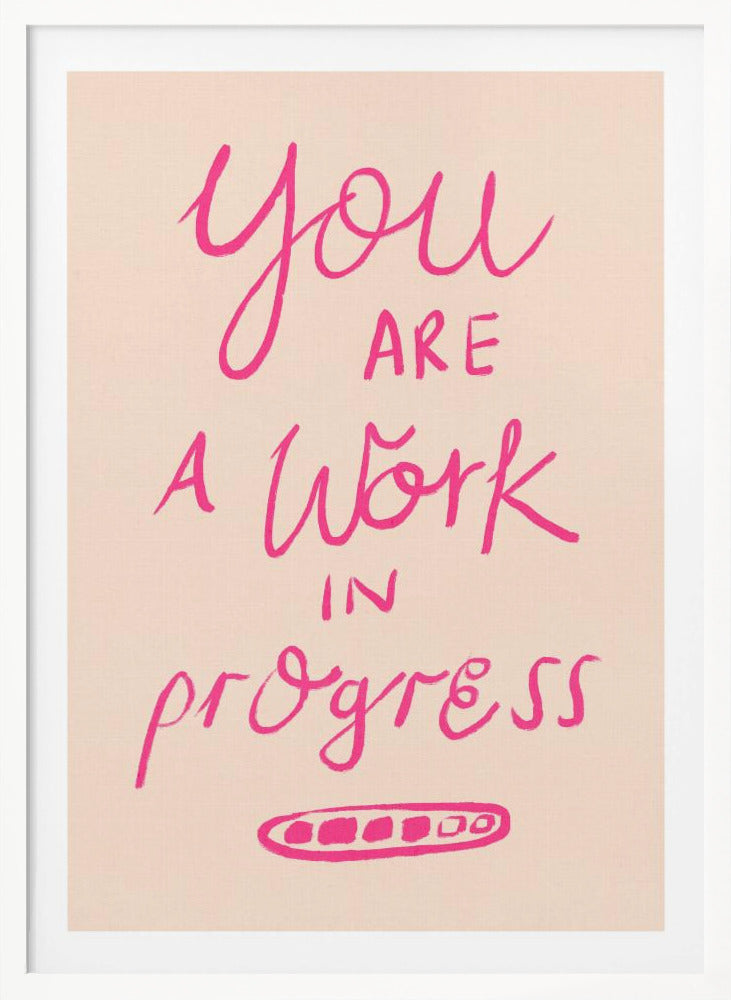 A framed art print featuring the motivational quote 'You are a work in progress'. The text is rendered in a vibrant pink, hand-lettered style against a soft beige background. The words 'You', 'a Work', and 'progress' are in a flowing script, while 'are' and 'in' are in a simple uppercase font. Wall Art