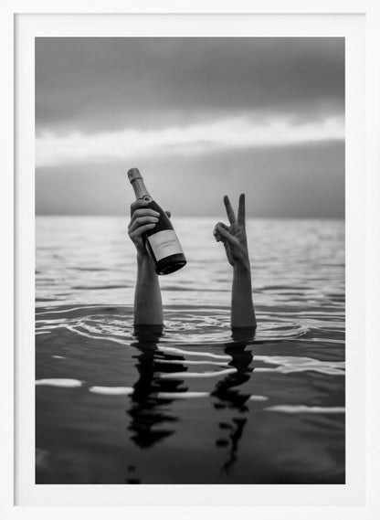 A black and white vertical photograph showing two arms sticking out of calm water. One hand holds a bottle of champagne, while the other makes a peace sign, all under a cloudy sky. Poster