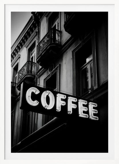 A dramatic, low-angle, black and white photograph of a bright white neon sign that reads 'COFFEE', mounted on a classic-style building with ornate balconies. Print