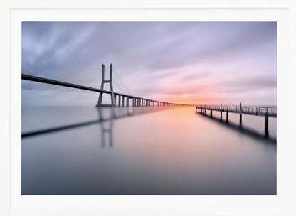A serene long-exposure photograph of a modern cable-stayed bridge and a pier stretching over mirror-like water at sunset. The sky is filled with soft, streaky clouds in hues of pink and purple, reflected on the calm water's surface, all enclosed in a silver frame. Decor