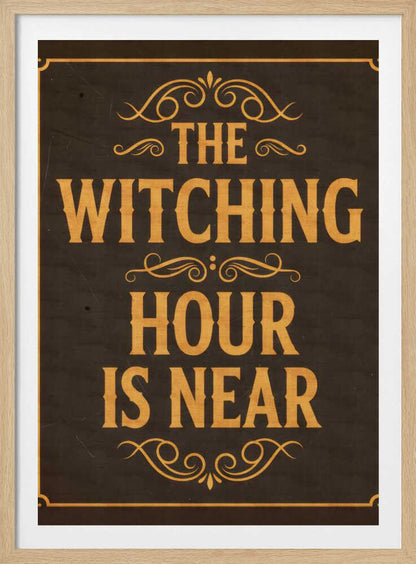 A framed vintage-style sign with a dark brown, distressed background. In a bold, golden-yellow serif font, the text reads 'THE WITCHING HOUR IS NEAR'. The text is adorned with ornate, swirling flourishes above, between, and below the lines. A thin golden-yellow border frames the entire design. Poster