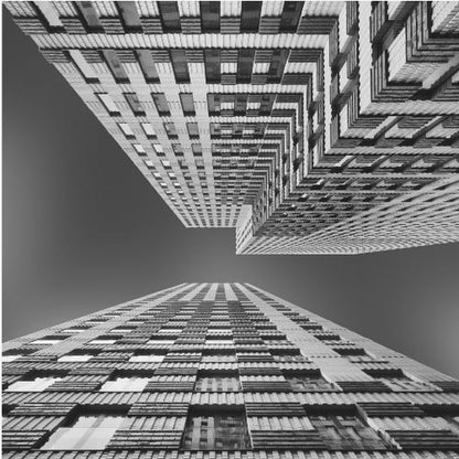 A framed, black and white, low-angle photograph looking up between two towering skyscrapers, creating a dramatic perspective with geometric patterns against a dark sky. Poster
