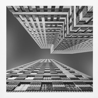 A framed, black and white, low-angle photograph looking up between two towering skyscrapers, creating a dramatic perspective with geometric patterns against a dark sky. Poster