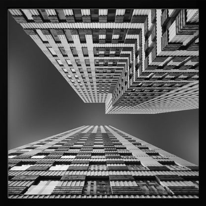 A framed, black and white, low-angle photograph looking up between two towering skyscrapers, creating a dramatic perspective with geometric patterns against a dark sky. Poster
