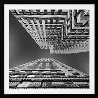 A framed, black and white, low-angle photograph looking up between two towering skyscrapers, creating a dramatic perspective with geometric patterns against a dark sky. Poster