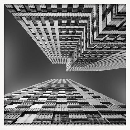 A framed, black and white, low-angle photograph looking up between two towering skyscrapers, creating a dramatic perspective with geometric patterns against a dark sky. Poster