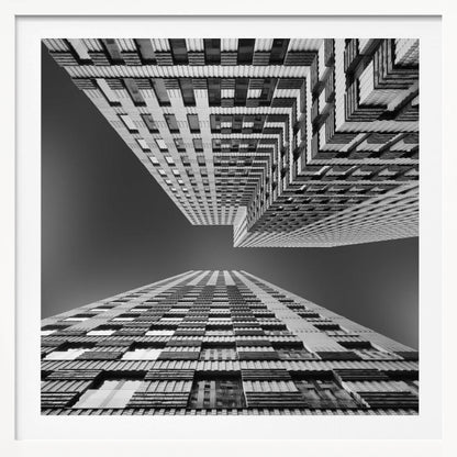A framed, black and white, low-angle photograph looking up between two towering skyscrapers, creating a dramatic perspective with geometric patterns against a dark sky. Poster