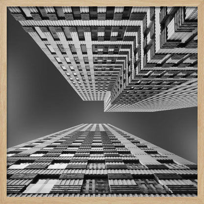A framed, black and white, low-angle photograph looking up between two towering skyscrapers, creating a dramatic perspective with geometric patterns against a dark sky. Poster