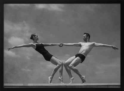 A black and white photograph of a male and female ballet dancer striking a symmetrical, athletic pose on a ledge. They hold hands, leaning away from each other in a display of strength and balance against a cloudy sky, all enclosed within a silver frame. Print