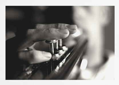 A dramatic, close-up, black and white photograph of a musician's fingers pressing down on the silver valves of a trumpet, with a soft, out-of-focus background. The image is enclosed in a brushed silver frame. Poster