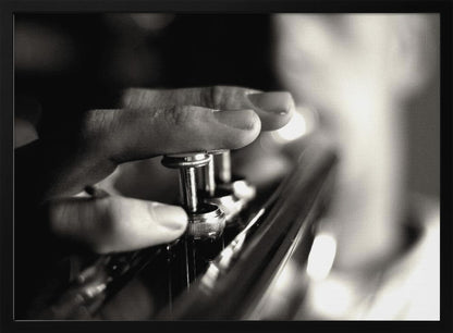 A dramatic, close-up, black and white photograph of a musician's fingers pressing down on the silver valves of a trumpet, with a soft, out-of-focus background. The image is enclosed in a brushed silver frame. Poster