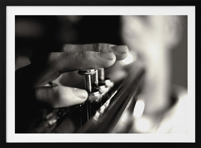 A dramatic, close-up, black and white photograph of a musician's fingers pressing down on the silver valves of a trumpet, with a soft, out-of-focus background. The image is enclosed in a brushed silver frame. Poster
