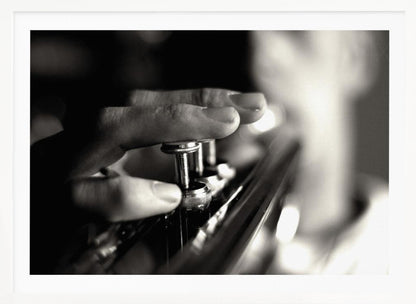 A dramatic, close-up, black and white photograph of a musician's fingers pressing down on the silver valves of a trumpet, with a soft, out-of-focus background. The image is enclosed in a brushed silver frame. Poster