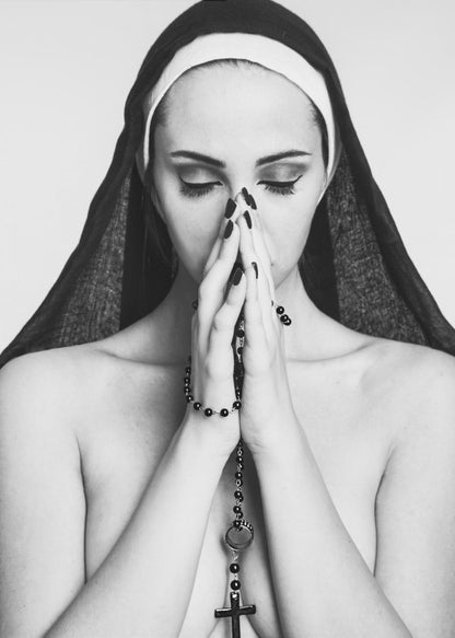 A black and white portrait of a woman with dramatic eye makeup wearing a nun's habit. Her eyes are closed and her hands are clasped in front of her face in prayer, holding a black rosary. Her shoulders are bare, creating a stark contrast. Artwork