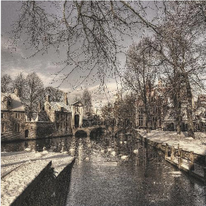A vintage-style, framed photograph of a European canal scene in winter. Historic buildings and bare trees line the partially frozen canal, where several white swans are swimming. A light dusting of snow covers the canal banks and rooftops under a cloudy sky. Wall Art