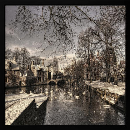 A vintage-style, framed photograph of a European canal scene in winter. Historic buildings and bare trees line the partially frozen canal, where several white swans are swimming. A light dusting of snow covers the canal banks and rooftops under a cloudy sky. Wall Art