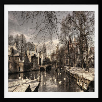A vintage-style, framed photograph of a European canal scene in winter. Historic buildings and bare trees line the partially frozen canal, where several white swans are swimming. A light dusting of snow covers the canal banks and rooftops under a cloudy sky. Wall Art