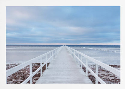 A framed photograph capturing a long, white wooden pier from a central perspective, leading the eye across a calm, icy sea towards the distant horizon under a cloudy blue sky. Print