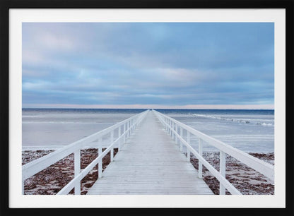 A framed photograph capturing a long, white wooden pier from a central perspective, leading the eye across a calm, icy sea towards the distant horizon under a cloudy blue sky. Print